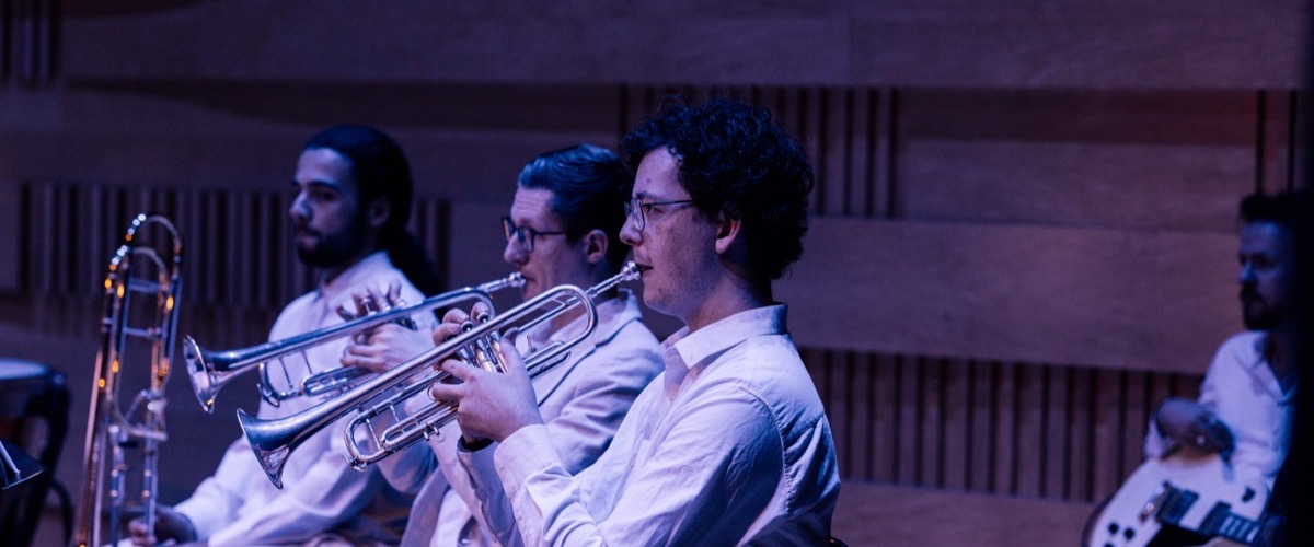 A group of musicians seated in a row, each playing a brass instrument.