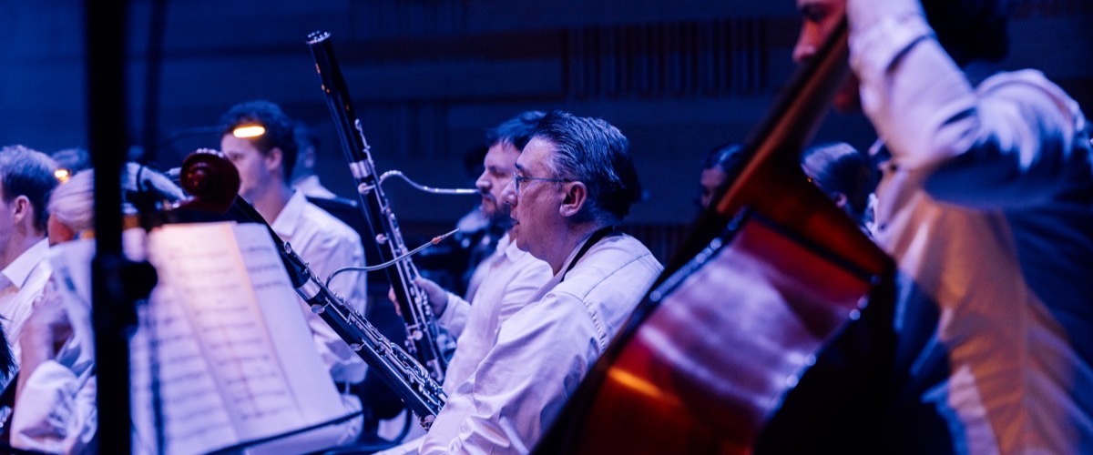 A group of musicians, possibly an orchestra, are playing various instruments in a dimly lit room.
