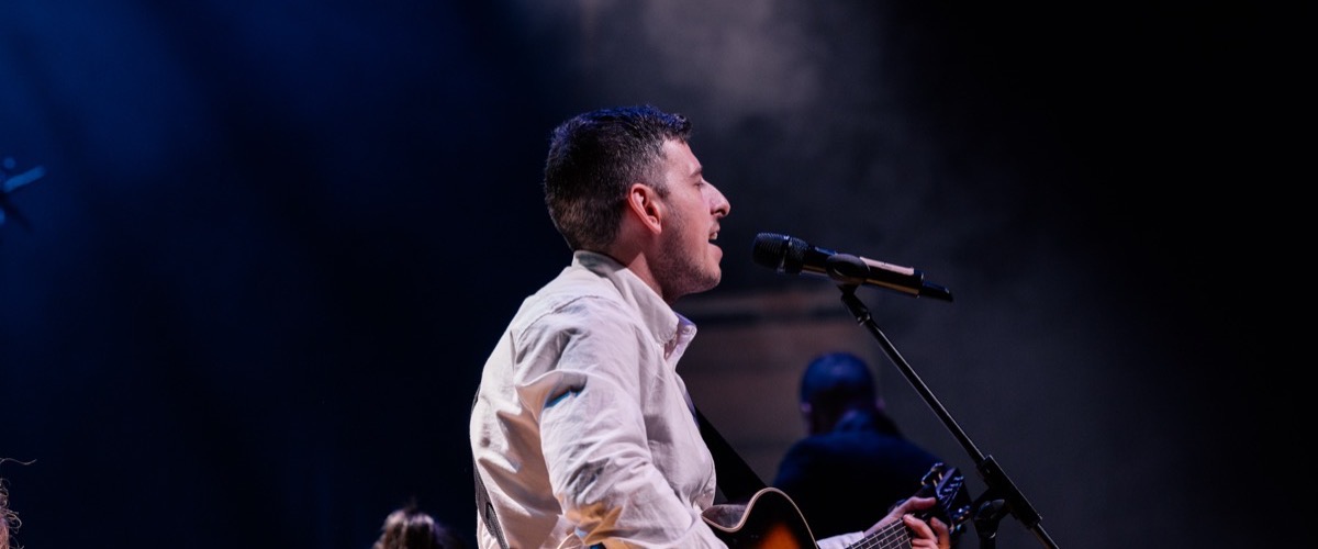 A man playing guitar and singing into a microphone on stage.