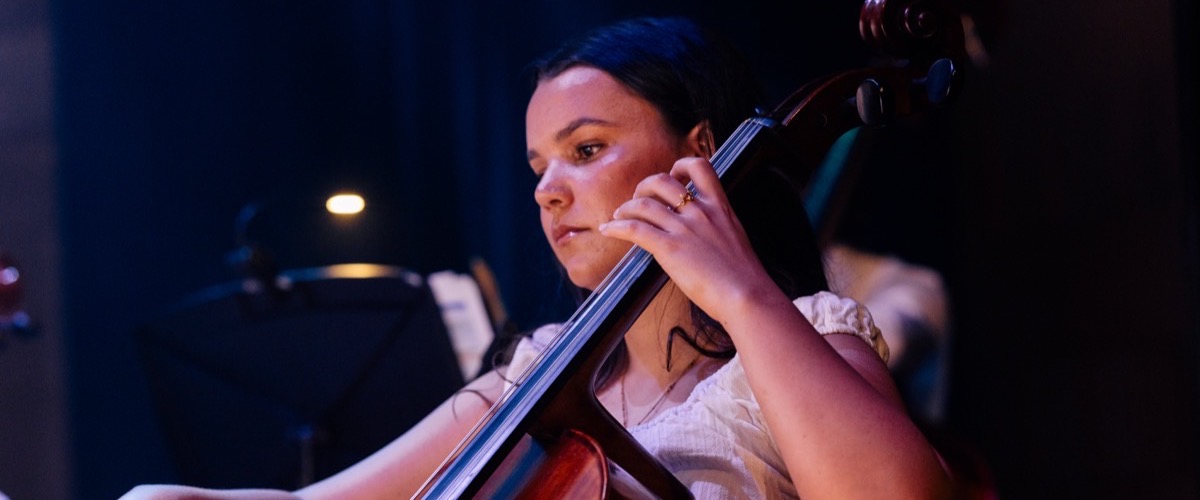 A woman playing a cello in a dimly lit room.