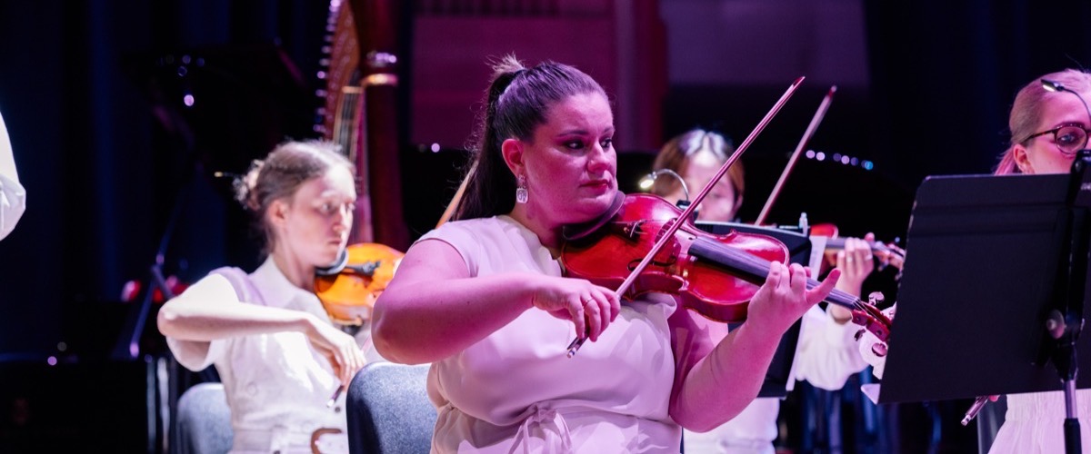 A woman is playing a violin in a group of musicians on stage.