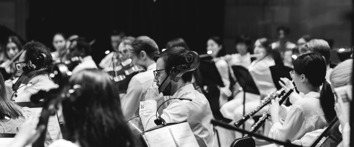 This black-and-white photograph depicts a large ensemble of musicians playing various instruments in unison.