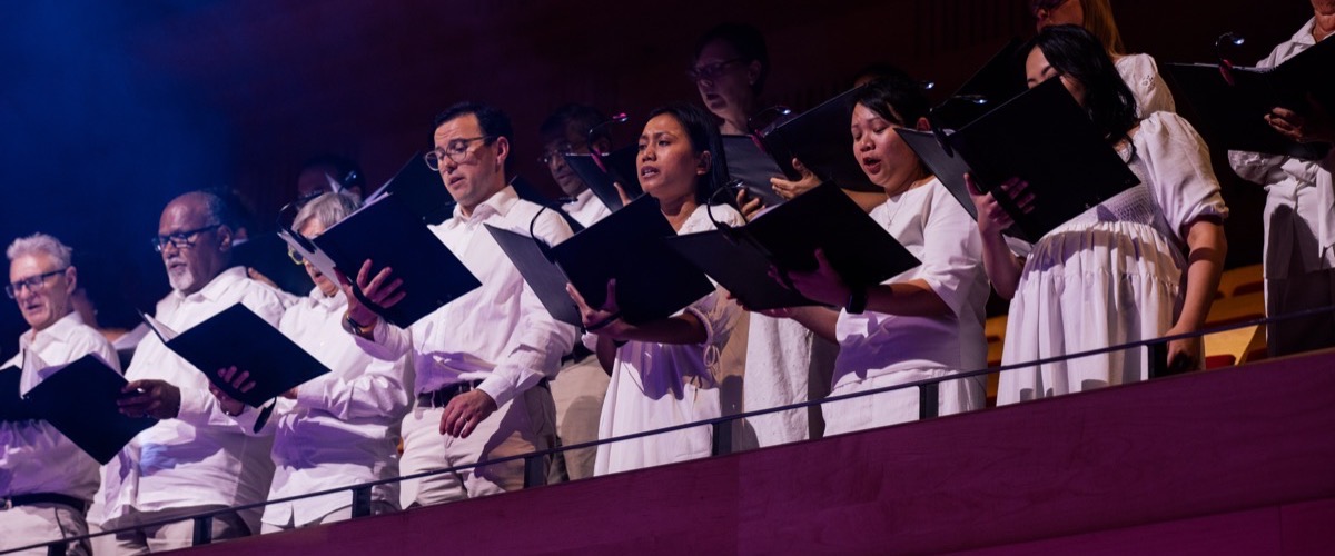 A group of people in white clothing are singing and holding black songbooks.