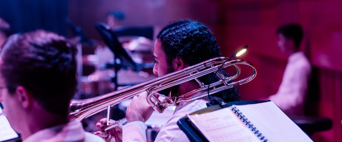 A man playing a trombone in an orchestra or band, with a music stand in front of him.