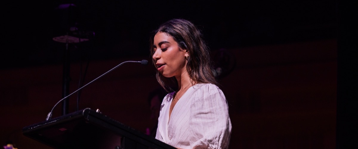 Graph shows a woman standing at a microphone, wearing a white shirt with pinstripes.