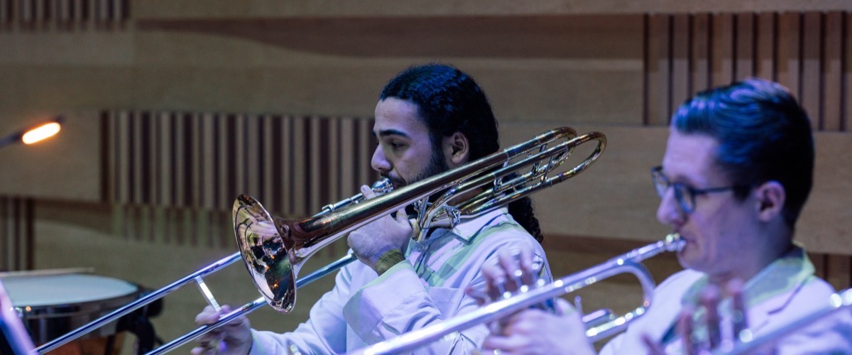 Two men playing trombones in a band or orchestra setting.