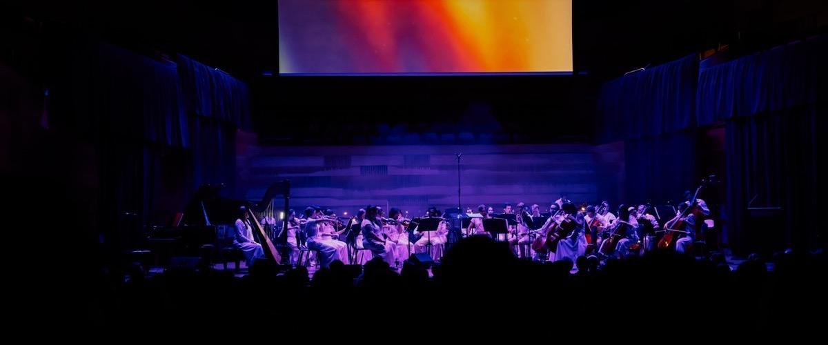 The photograph depicts a group of musicians performing on stage, surrounded by an audience.