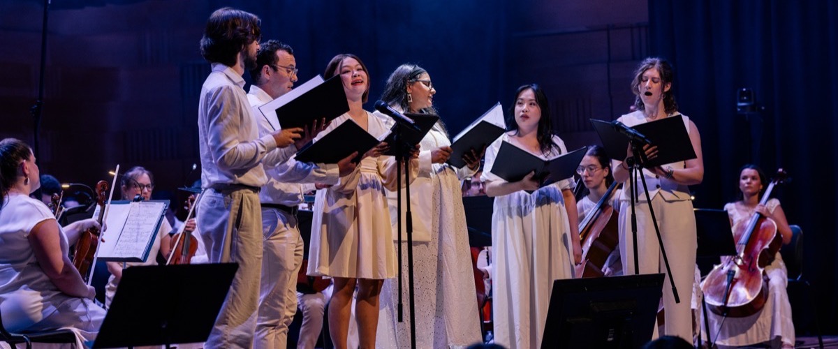 A group of people performing on stage, with a string orchestra in the background.