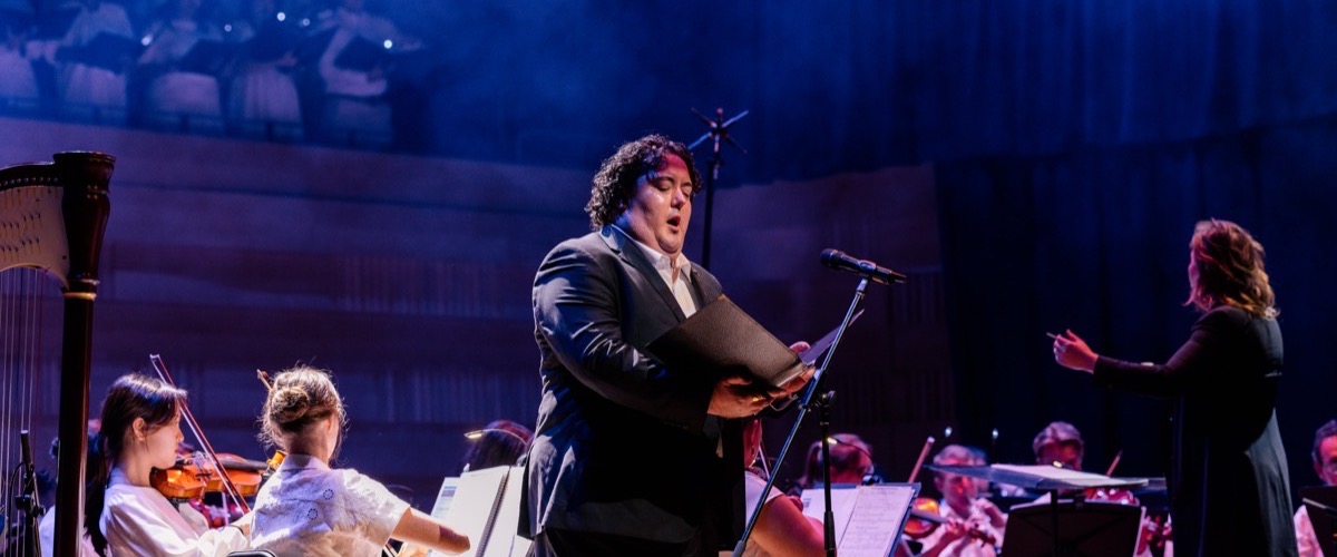 A man singing on stage with an orchestra in the background.