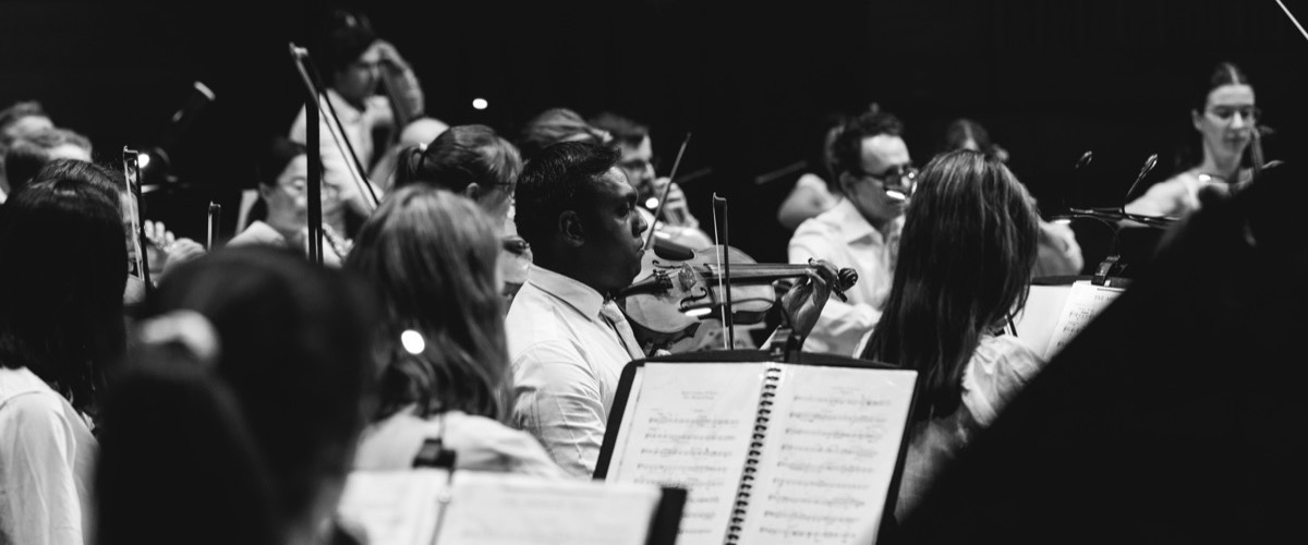 This black-and-white photograph depicts a group of musicians in white shirts holding musical instruments and sheet music.