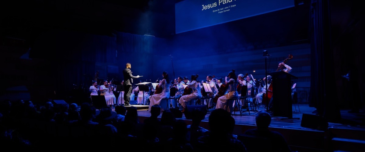 Graph depicts a symphony orchestra performing on a stage, with a conductor and musicians playing various instruments.