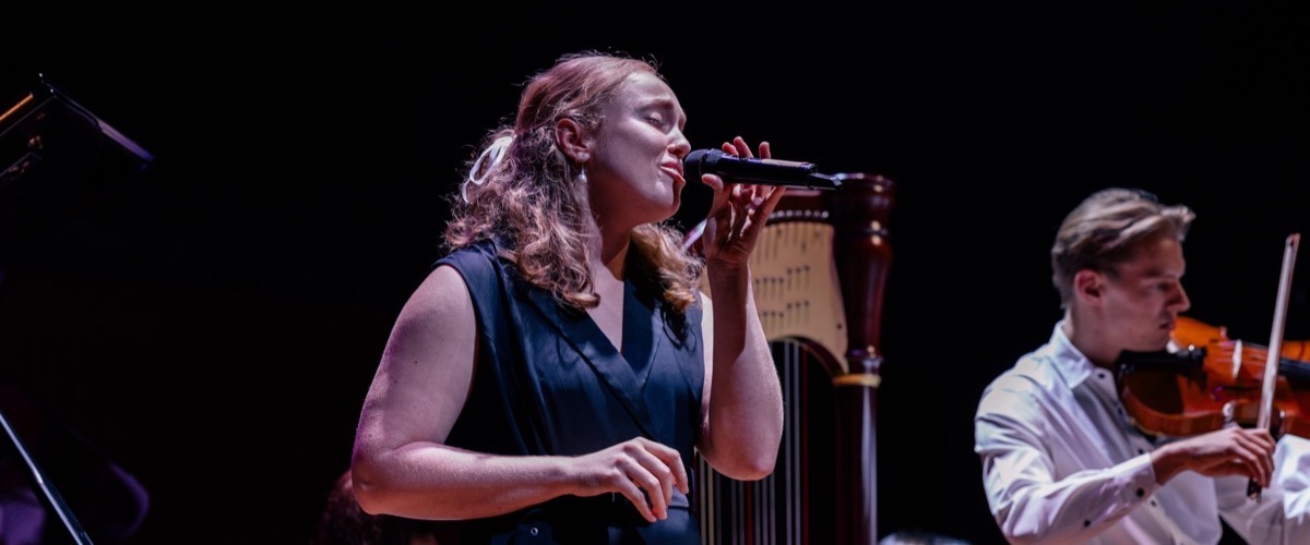 A woman singing into a microphone, accompanied by a man playing the violin.