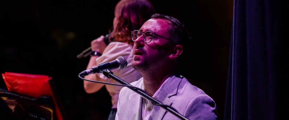 Graph depicts a man singing into a microphone on stage, accompanied by a woman playing a violin in the background.