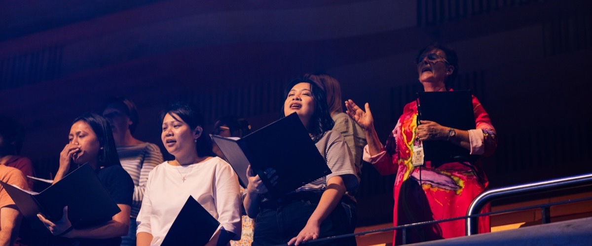 A group of women are singing together in a choir, holding music sheets.