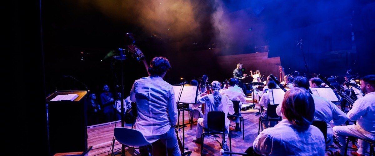 A group of musicians perform on stage, with a conductor leading the ensemble.