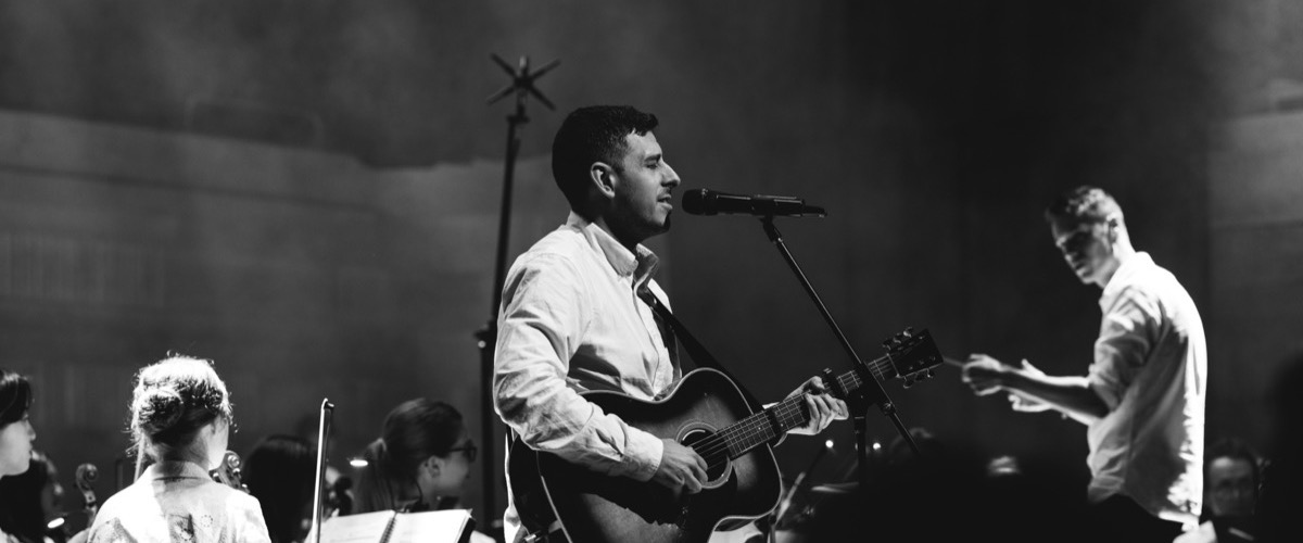 A man is playing a guitar while another man sings into a microphone.