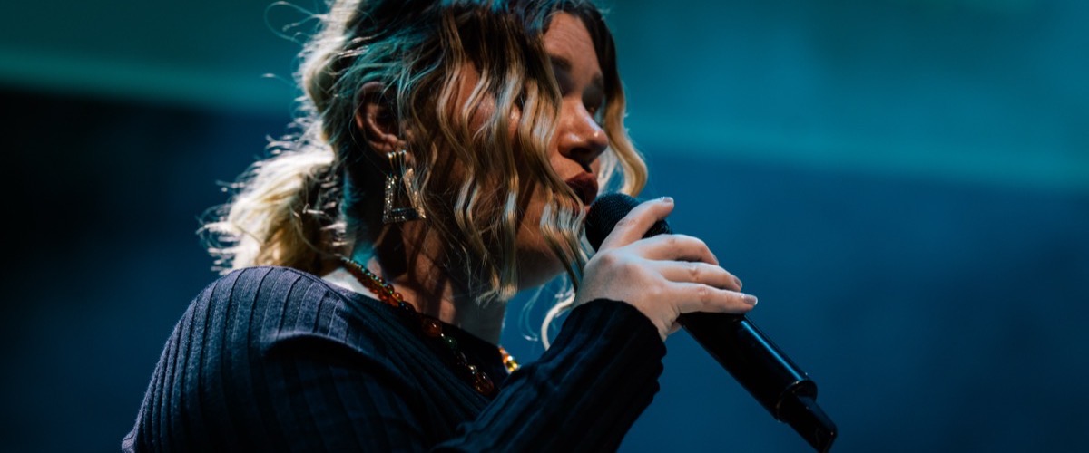 A woman holding a microphone, wearing a dark shirt and large dangling earrings.