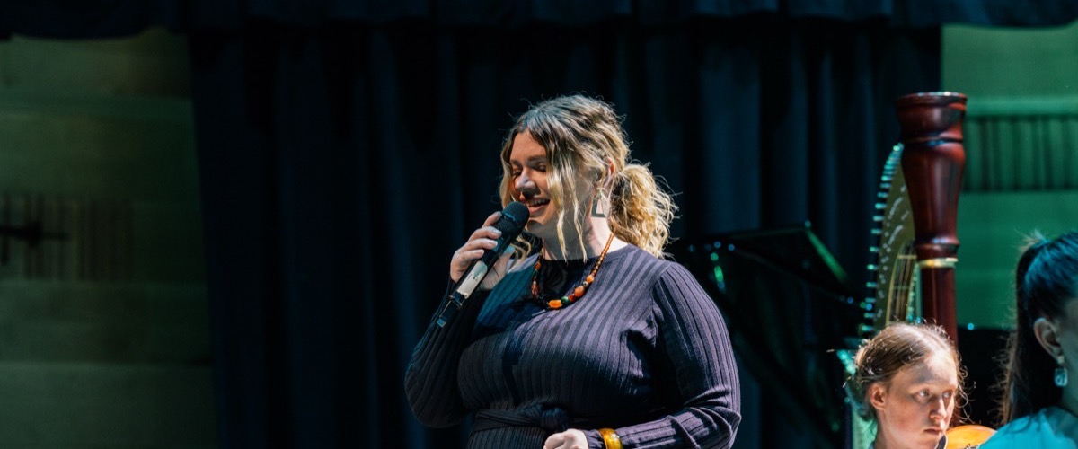 A woman holding a microphone in front of a harp.