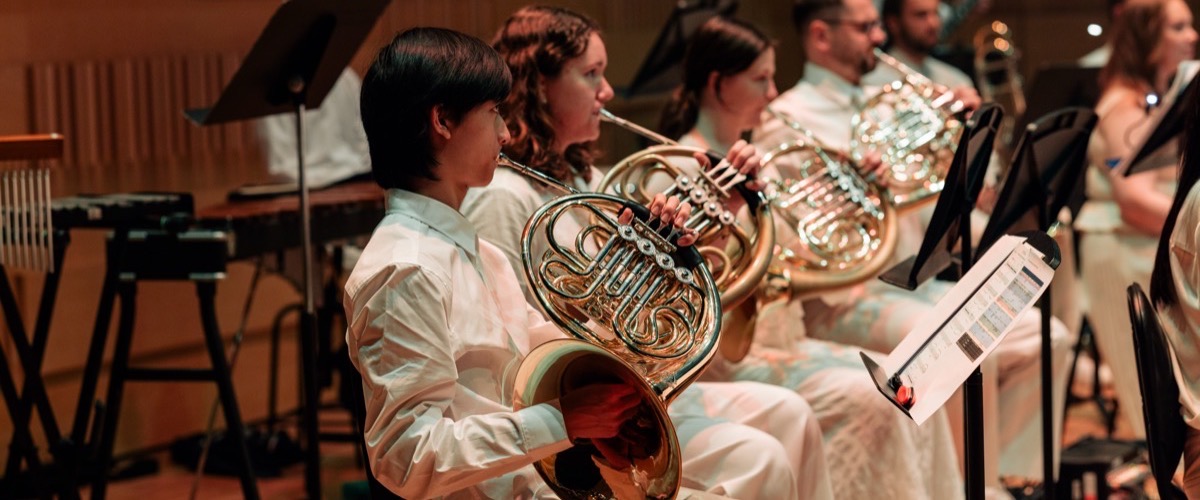 A group of musicians in white clothing are seated playing brass instruments.