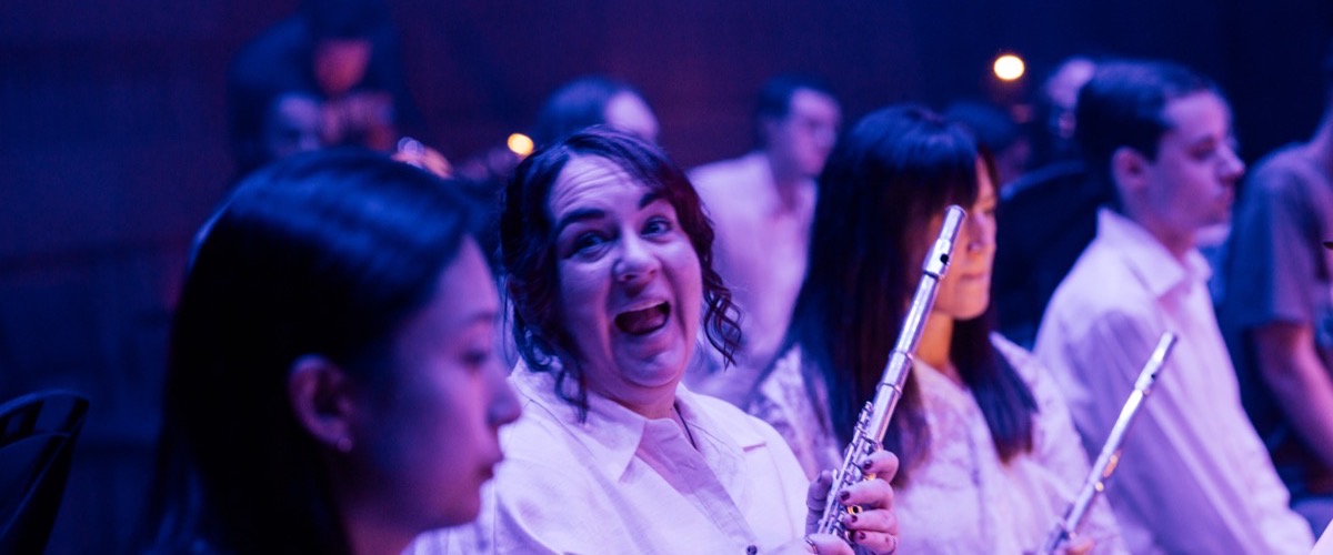 A group of people are gathered together, with one person holding a flute and wearing a white shirt.