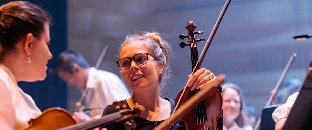 Graph depicts two women in an orchestra setting, one holding a cello and the other a violin.