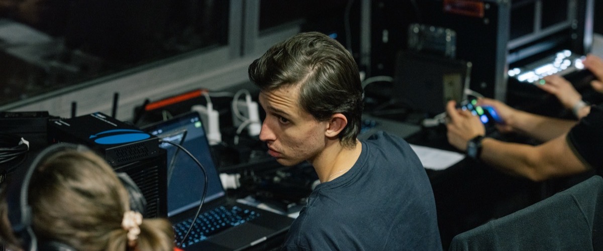 A man and woman sitting in front of laptops, surrounded by various electronic devices and cables.