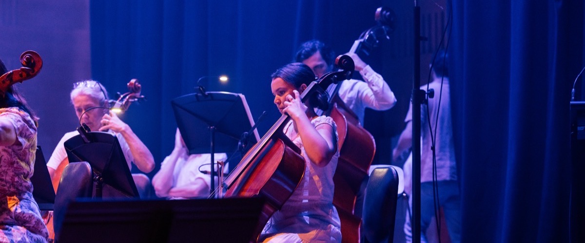 A group of musicians performing on stage, with a cellist prominently featured in the foreground.