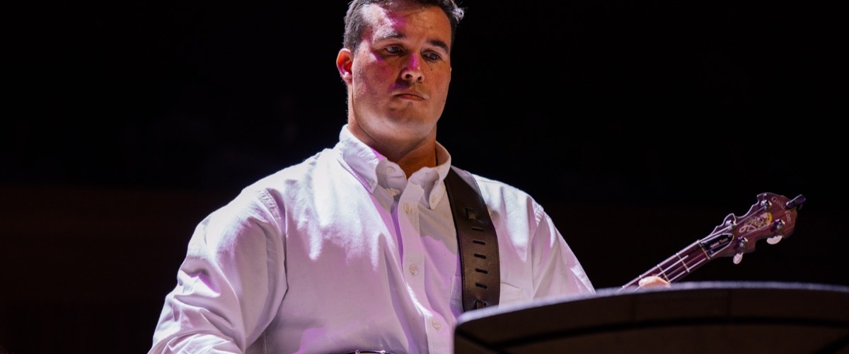 A man in a white shirt is playing a guitar with a black strap.