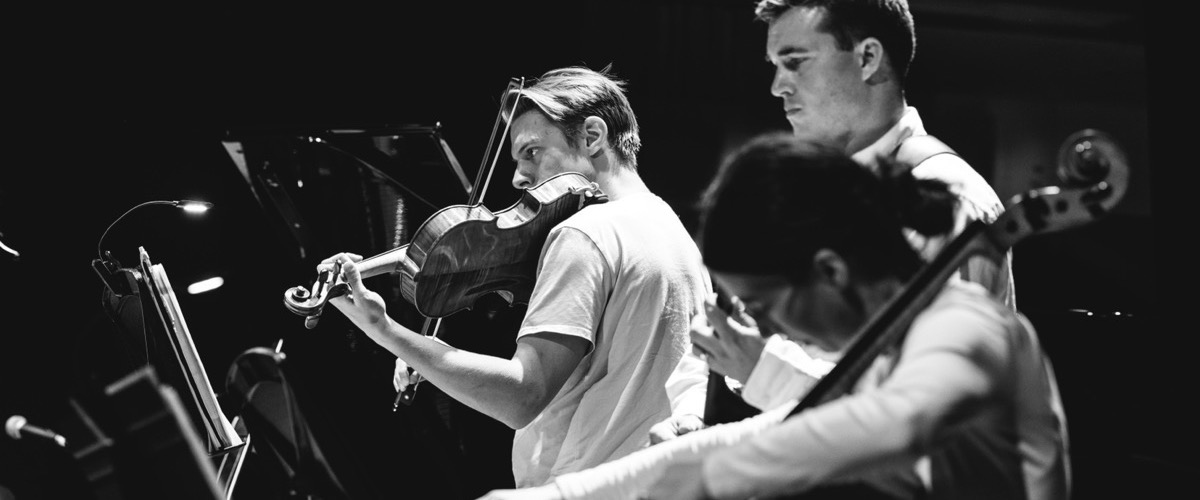 Three musicians in a dimly lit room, each playing a stringed instrument.