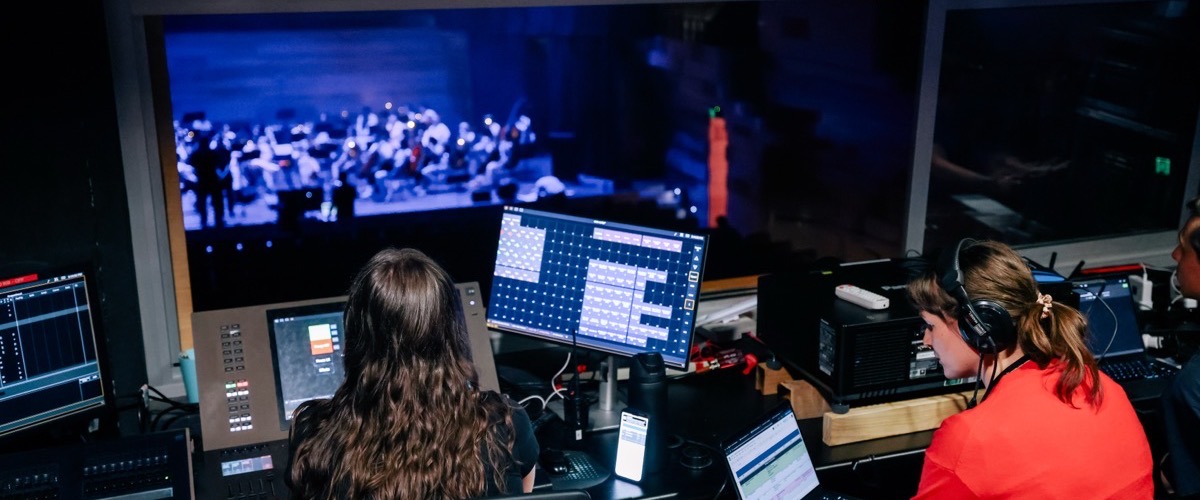 Two people working in a dark room with multiple computer screens.