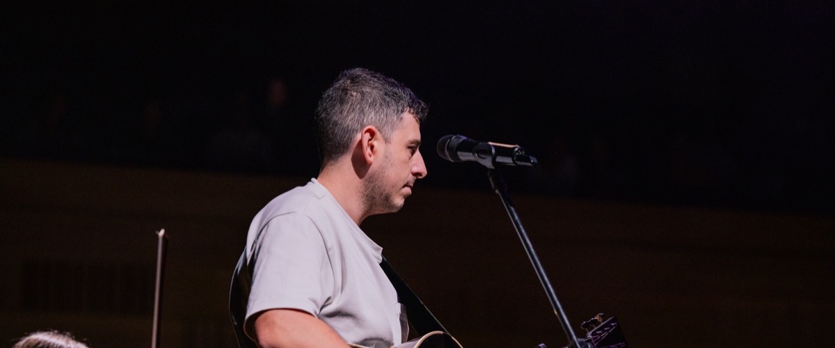 A man is performing on stage, holding a guitar and singing into a microphone.