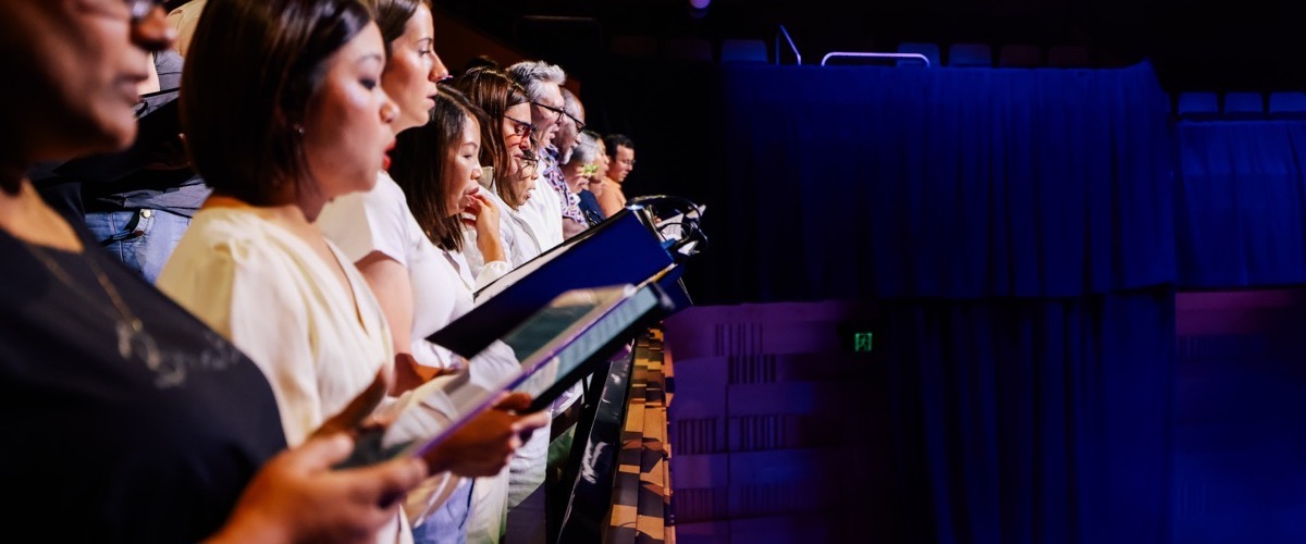 A group of people singing in a choir, with music stands in front of them.