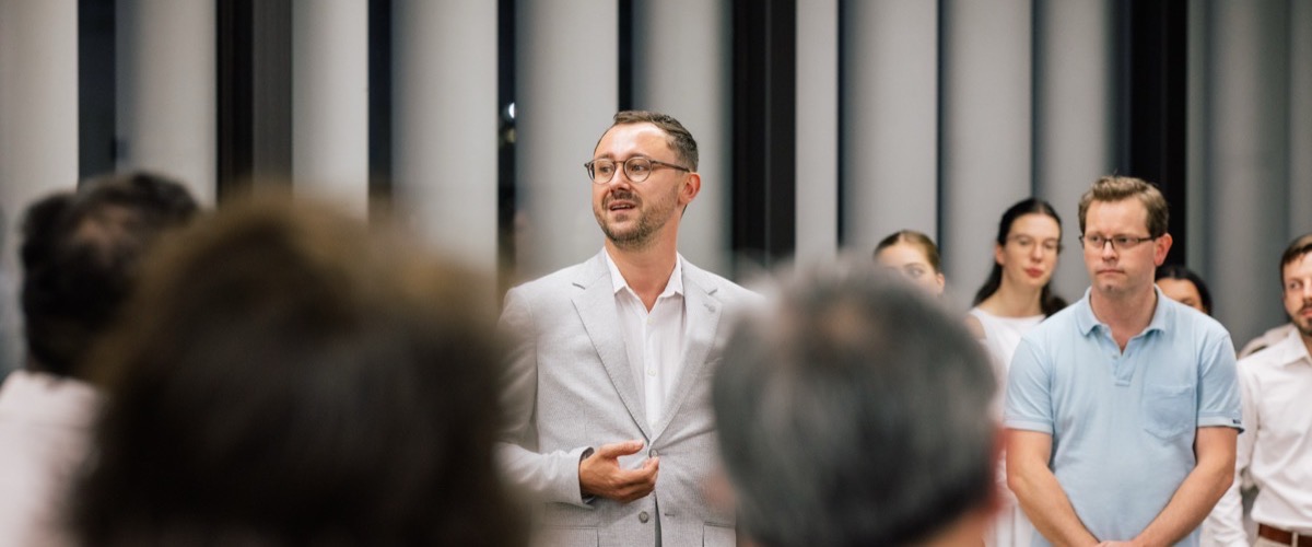 A man in a white suit jacket speaking to a group of people.