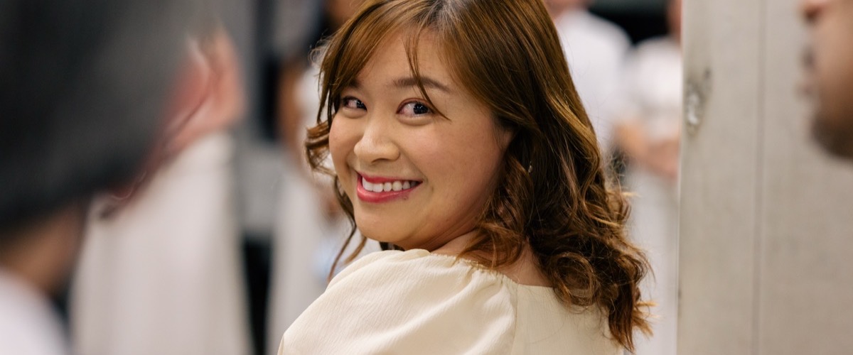 A woman with long brown hair, wearing a cream-colored top, facing the camera with a smile.