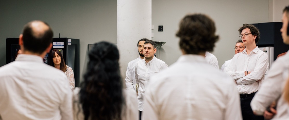 A group of people, mostly wearing white shirts, are gathered in a room with white walls.