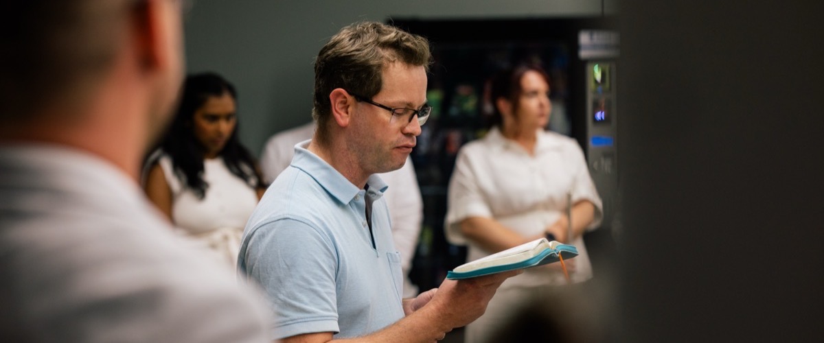 A man reading from an open notebook in a group setting.