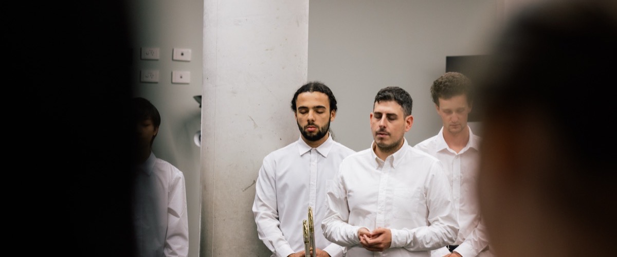 Four men standing in a room, wearing white shirts, with one holding a gold object.