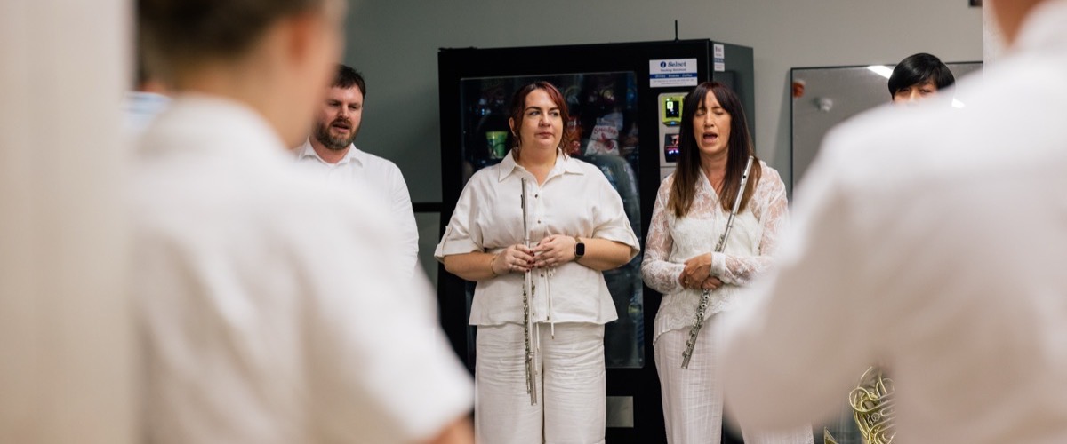 A group of people, mostly wearing white, are standing in a room with a vending machine in the background.