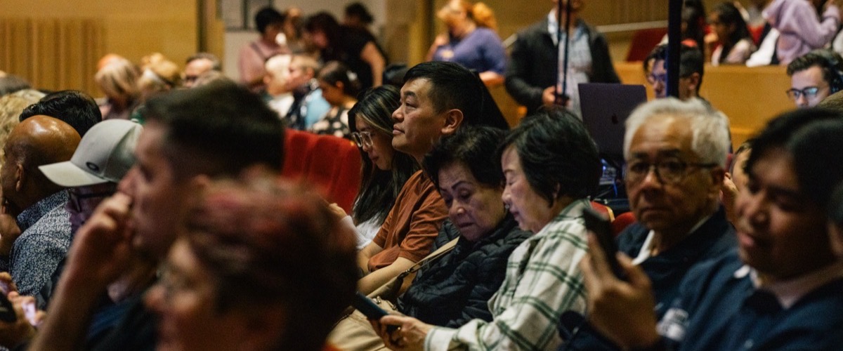 A crowd of people seated in an auditorium, with some individuals looking at their phones.