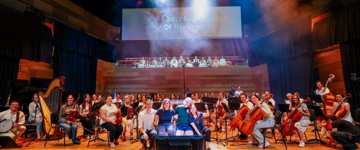 Graph depicts a group of musicians posing on a stage with a large screen displaying 'Easter Night Of Worship'.