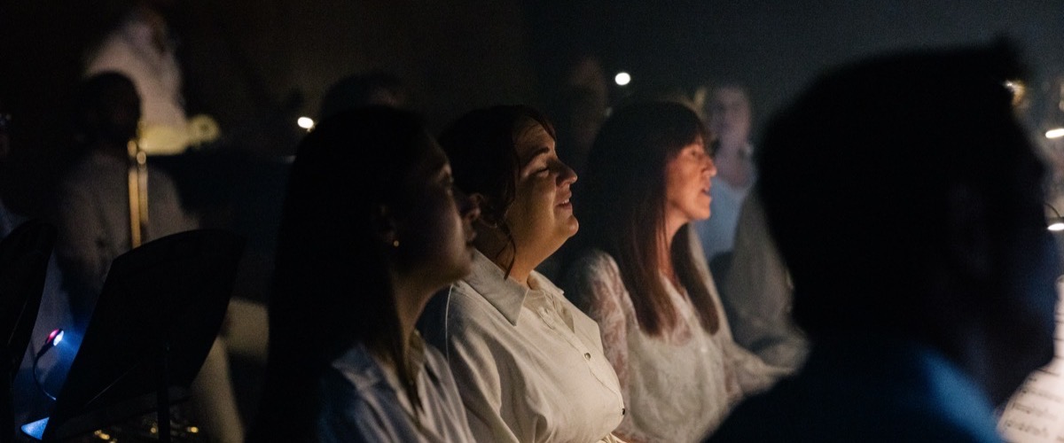 A group of women sitting in a dimly lit room, surrounded by others.