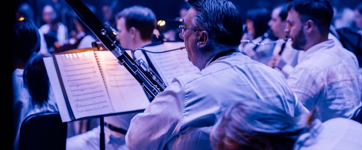 A man playing a clarinet in a band or orchestra, with sheet music in front of him.