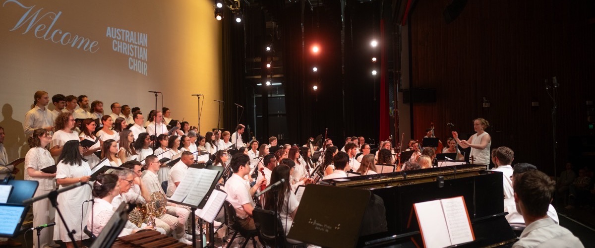 A large choir and orchestra on stage, with a projected "Welcome Australian Christian Choir" message.